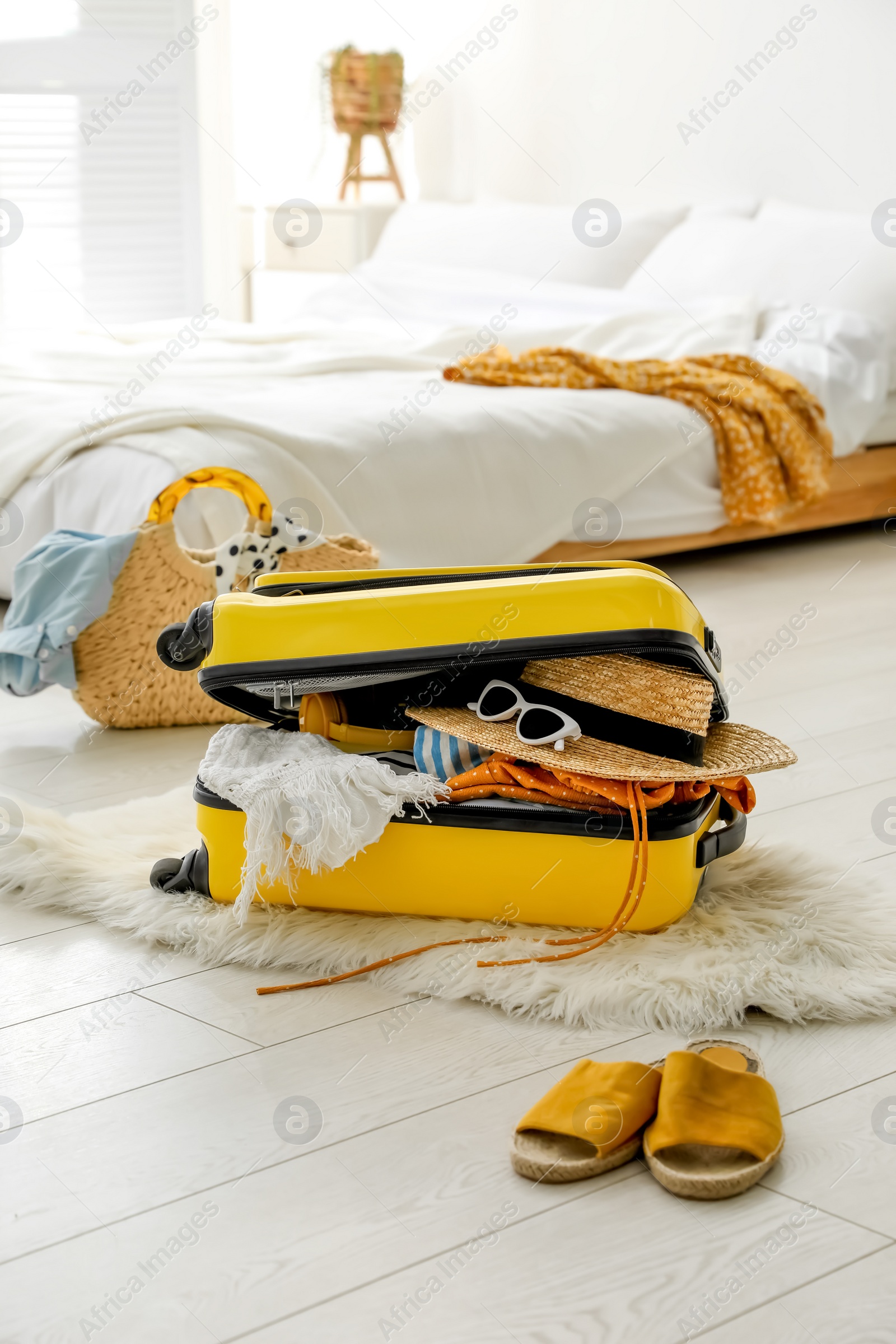 Photo of Open suitcase full of clothes, shoes and summer accessories on floor in room