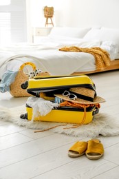 Photo of Open suitcase full of clothes, shoes and summer accessories on floor in room