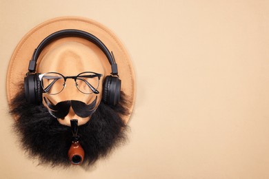 Photo of Man's face made of artificial mustache, beard, glasses and hat on beige background, top view. Space for text