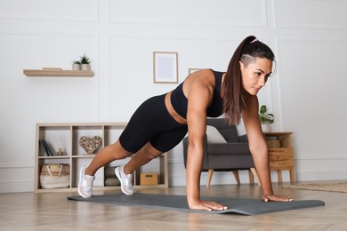 Young woman doing plank exercise on floor indoors