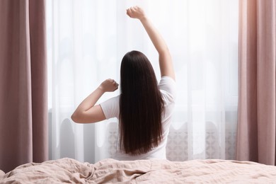 Photo of Woman stretching on bed at home, back view. Lazy morning