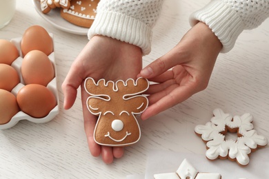 Woman holding delicious homemade Christmas cookie at white table, closeup