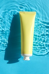 Tube with moisturizing cream in water on light blue background, top view