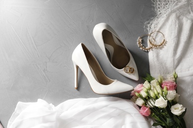 Flat lay composition with wedding dress, white high heel shoes and flowers on grey background. Space for text