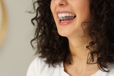 Photo of Young woman applying whitening strip on her teeth indoors, closeup. Space for text