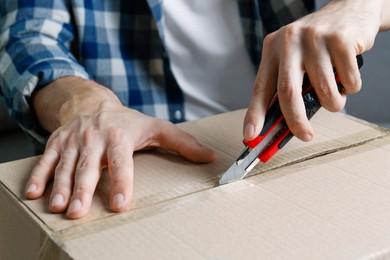 Photo of Man using utility knife to open parcel, closeup