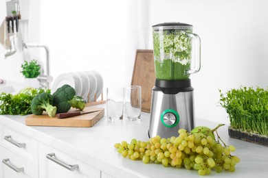 Blender with delicious smoothie and ingredients in kitchen