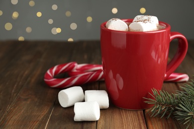Photo of Hot drink with marshmallows in red cup, fir branch and candy canes on wooden table