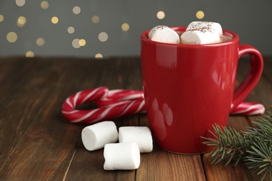 Hot drink with marshmallows in red cup, fir branch and candy canes on wooden table