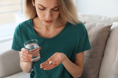 Photo of Upset young woman with abortion pill and glass of water at home, closeup