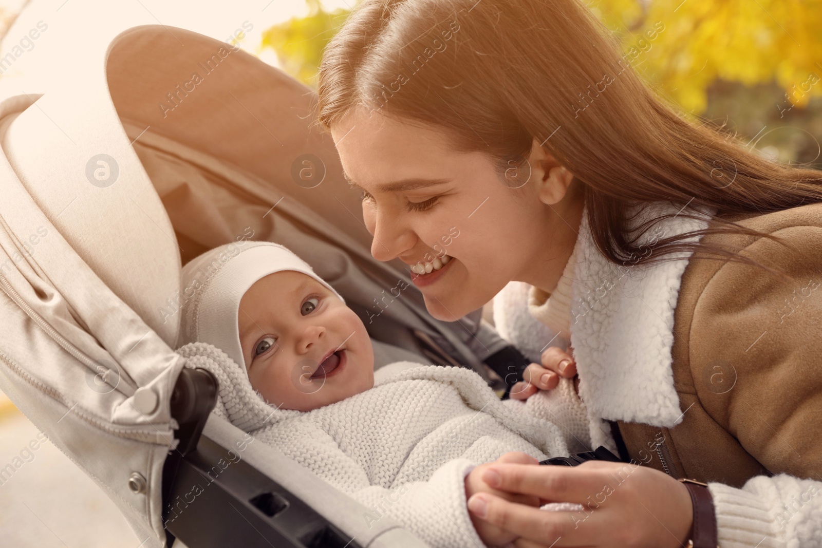 Photo of Happy mother with her baby daughter in stroller outdoors on autumn day