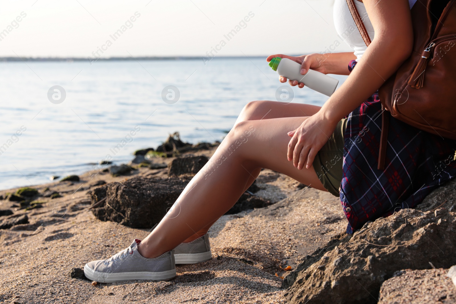 Photo of Woman applying insect repellent onto leg at beach, closeup. Space for text