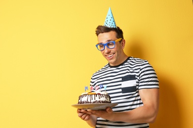 Photo of Young man with birthday cake on color background