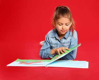 Cute little girl reading book on red background