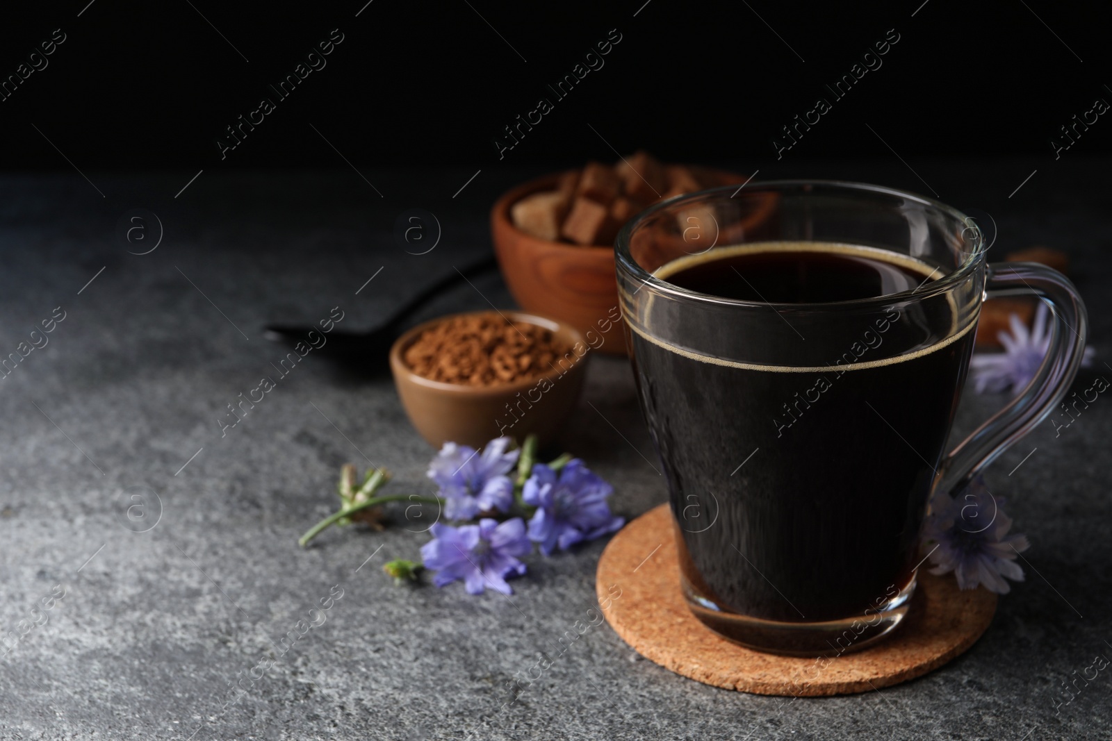 Photo of Glass cup of delicious chicory drink and flowers on grey table, space for text
