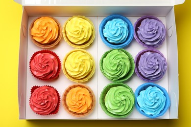 Tasty cupcakes in box on yellow background, top view