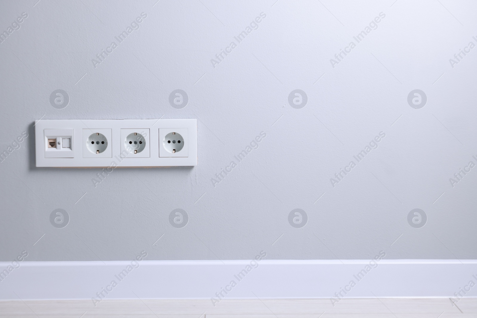 Photo of Electric power sockets on light grey wall indoors, space for text