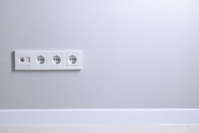 Electric power sockets on light grey wall indoors, space for text