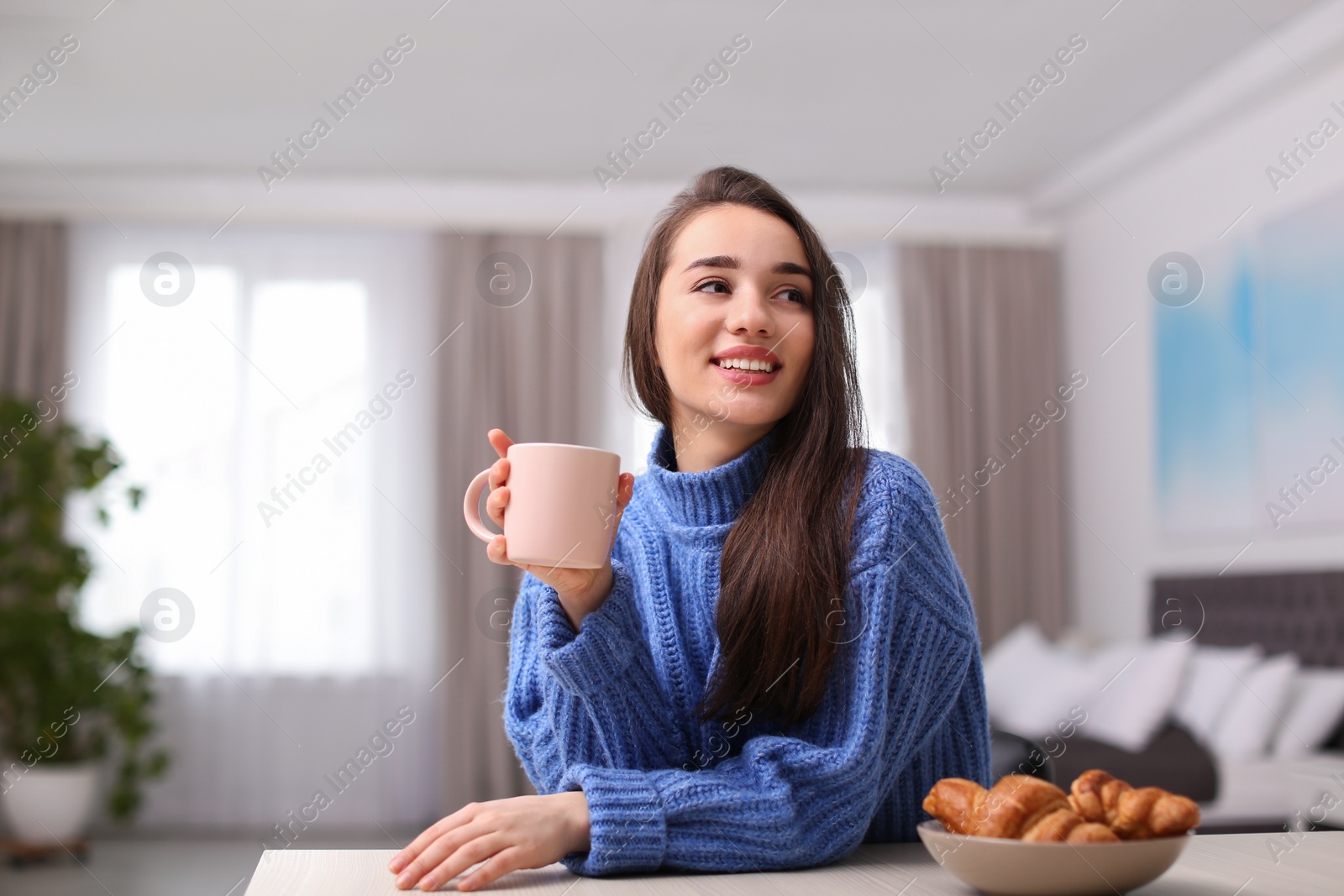 Photo of Young woman drinking coffee at table indoors. Winter season