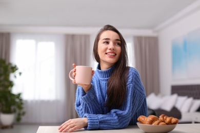 Photo of Young woman drinking coffee at table indoors. Winter season