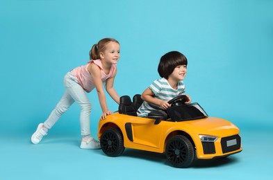 Cute girl pushing children's electric toy car with little boy on light blue background
