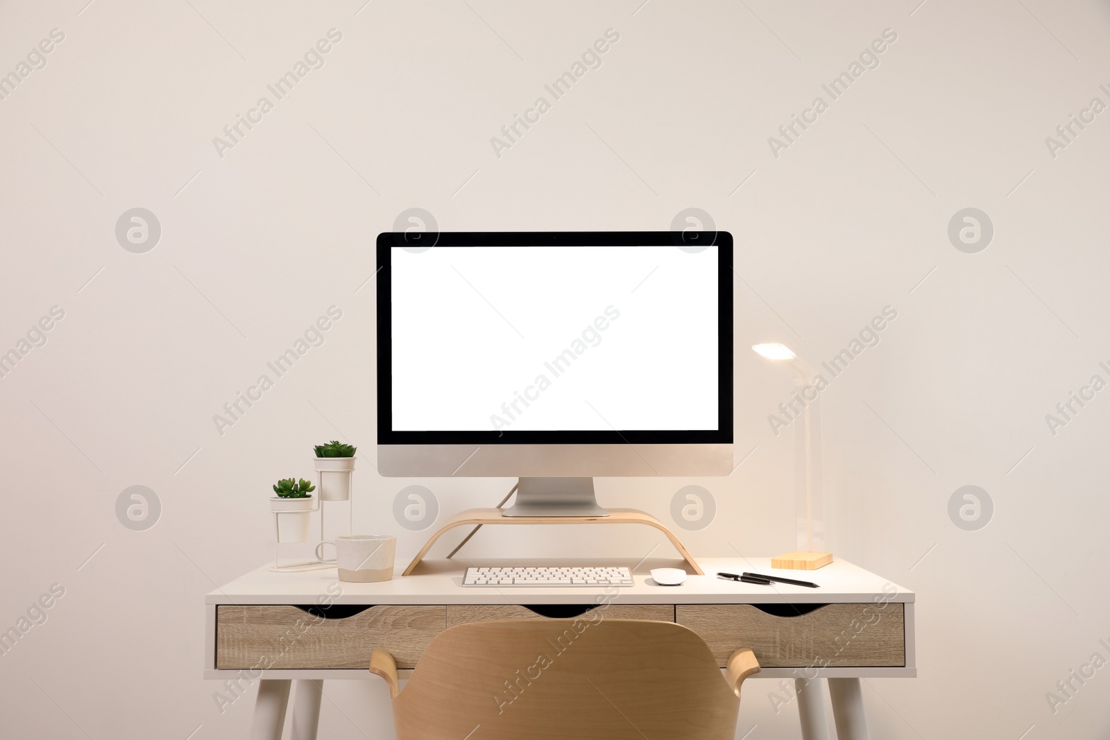 Photo of Comfortable workplace with blank computer display on desk near light wall. Space for text