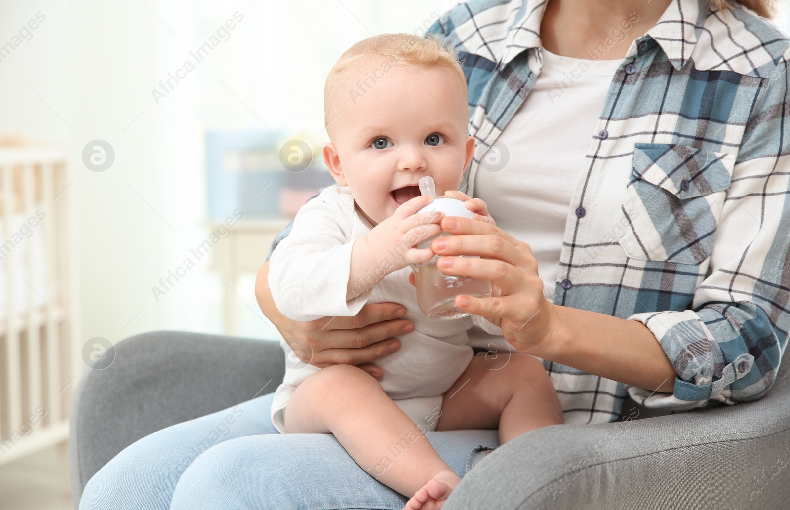 Photo of Lovely mother giving her baby drink from bottle in room