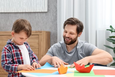 Photo of Dad and son making paper boats at coffee table indoors