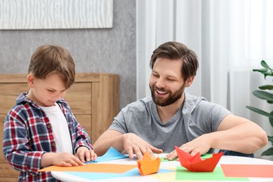 Dad and son making paper boats at coffee table indoors