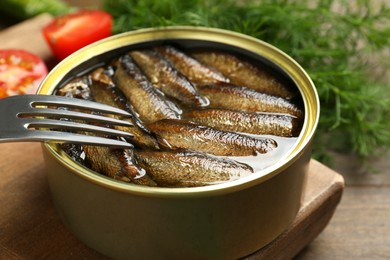 Tin can with tasty sprats and fork served on wooden table, closeup