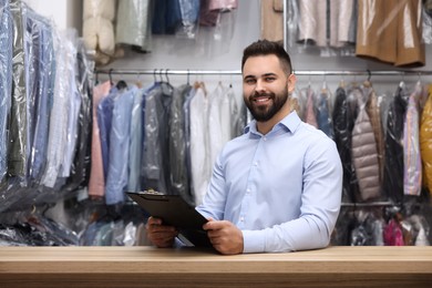 Dry-cleaning service. Happy worker holding clipboard at counter indoors