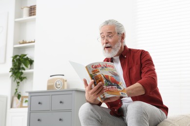 Senior man in eyeglasses reading magazine on bed at home, space for text