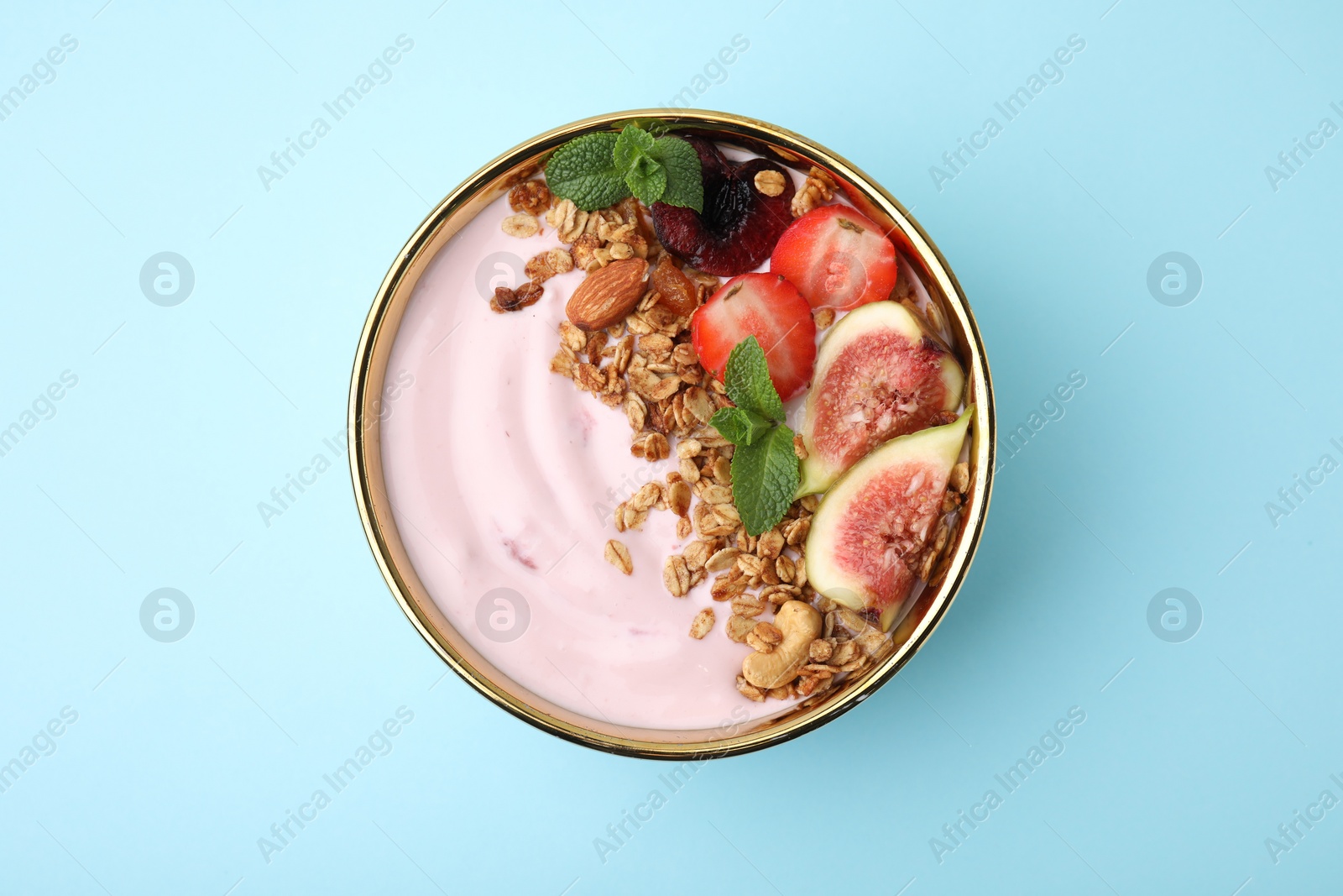 Photo of Bowl with yogurt, fruits and granola on light blue background, top view