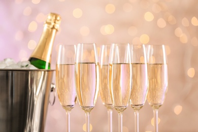 Photo of Glasses with champagne and bottle in bucket against blurred lights