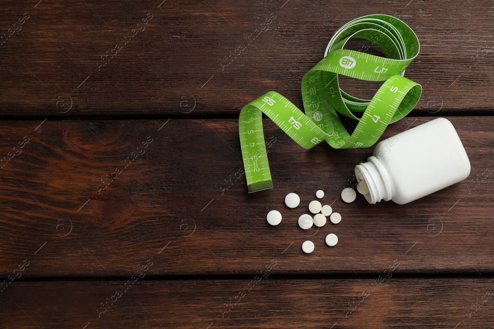 Photo of Jar of weight loss pills and measuring tape on wooden table, flat lay. Space for text