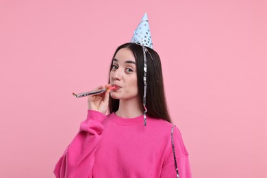 Woman in party hat with blower and streamers on pink background