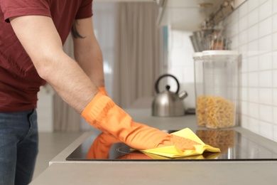 Young man cleaning oven cooktop with rag in kitchen, closeup