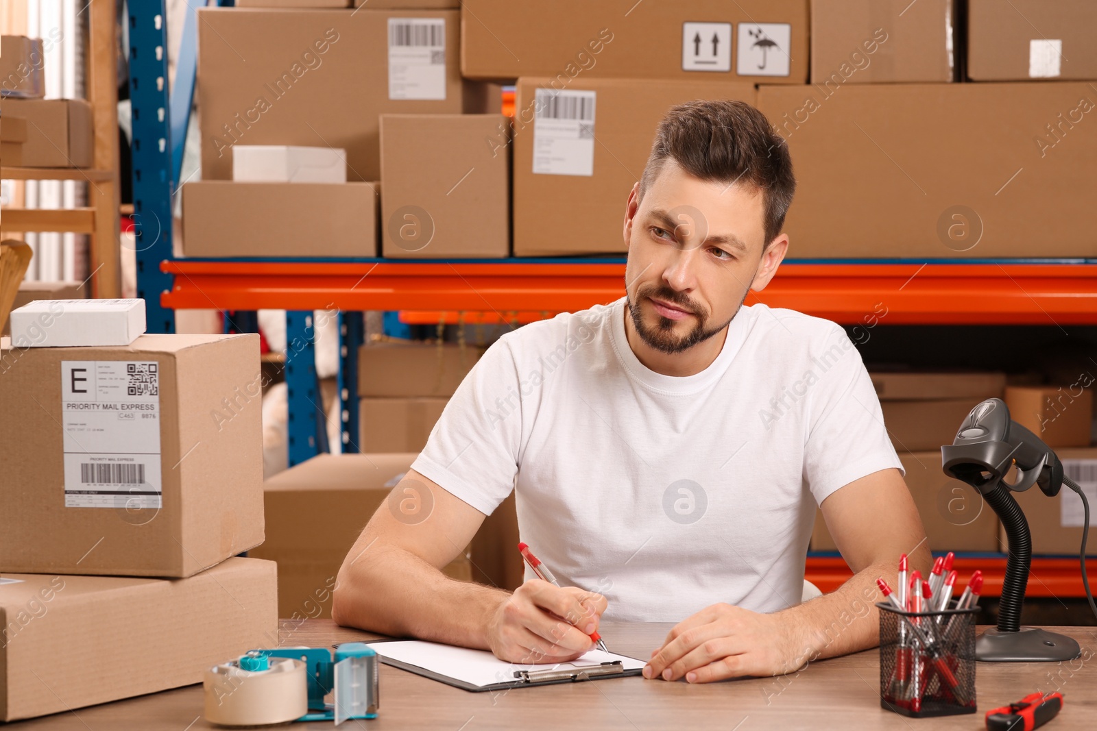 Photo of Post office worker with clipboard and parcels at counter indoors