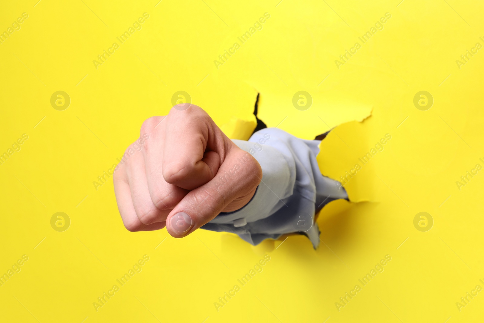 Photo of Businessman breaking through yellow paper with fist, closeup