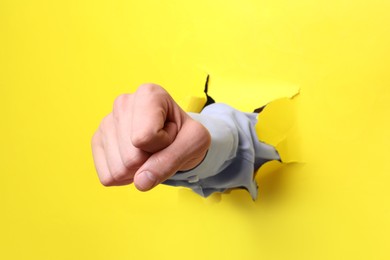 Businessman breaking through yellow paper with fist, closeup