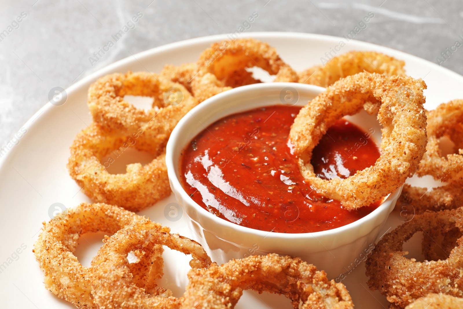 Photo of Homemade crunchy fried onion rings with sauce on table, closeup