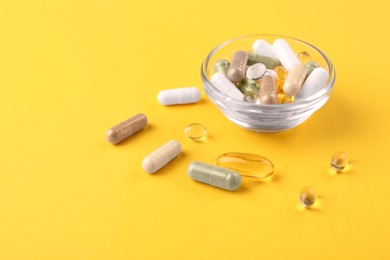 Photo of Different vitamin pills in glass bowl on yellow background, closeup. Space for text