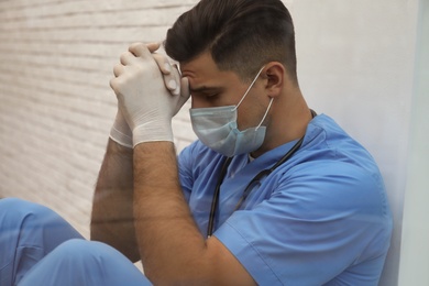 Sad doctor near window, view from outdoors. Stress of health care workers during coronavirus pandemic