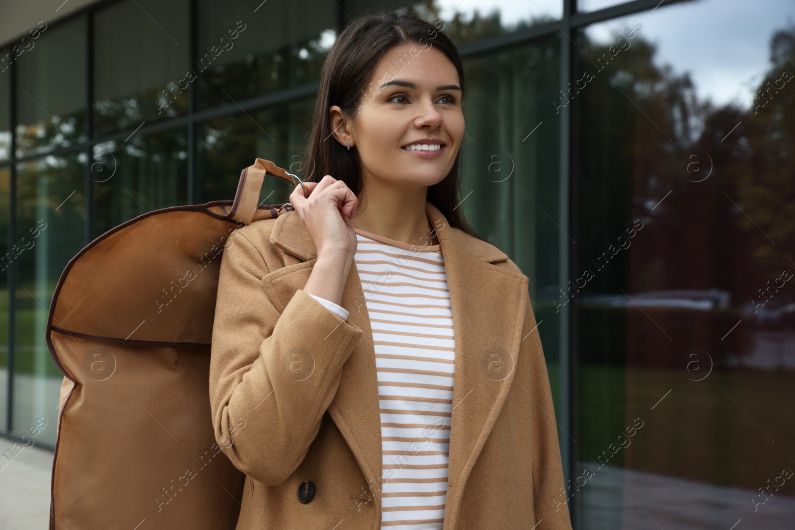 Photo of Attractive happy woman holding garment cover with clothes outdoors. Dry cleaning service