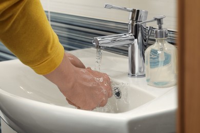 Photo of Man using water tap to rinse soap off hands in bathroom, closeup