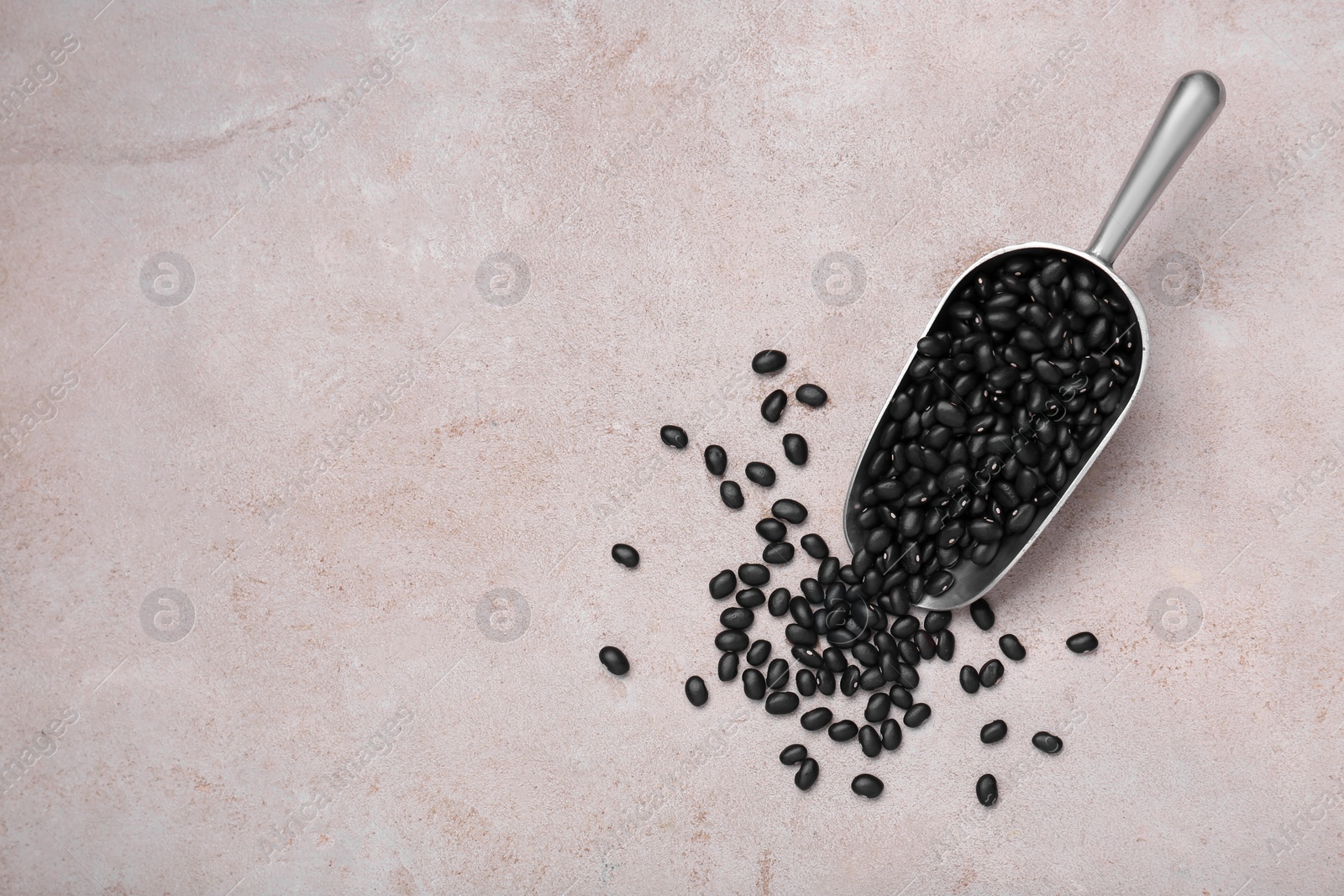 Photo of Scoop of raw black beans on light grey table, top view. Space for text