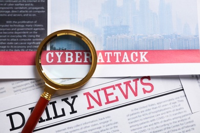 Newspaper with headline CYBER ATTACK and magnifying glass, top view