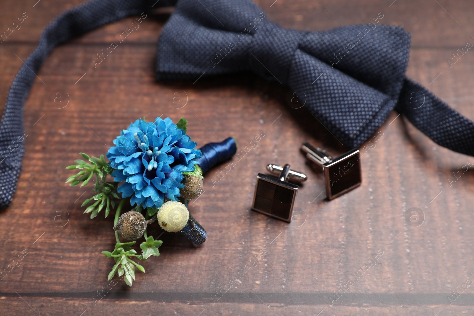 Photo of Wedding stuff. Stylish boutonniere, bow tie and cufflinks on wooden background, closeup