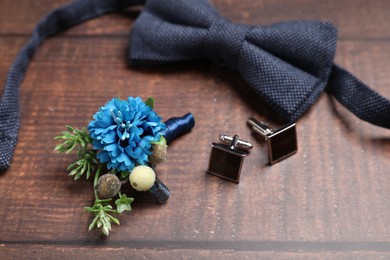 Wedding stuff. Stylish boutonniere, bow tie and cufflinks on wooden background, closeup