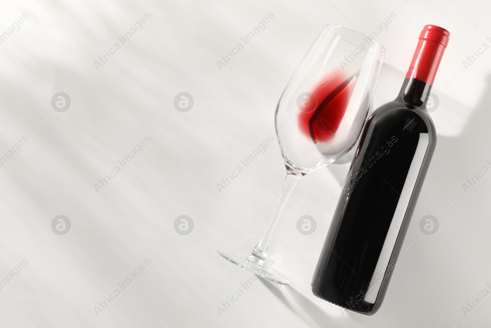 Photo of Bottle of expensive red wine and wineglass on light background, top view. Space for text